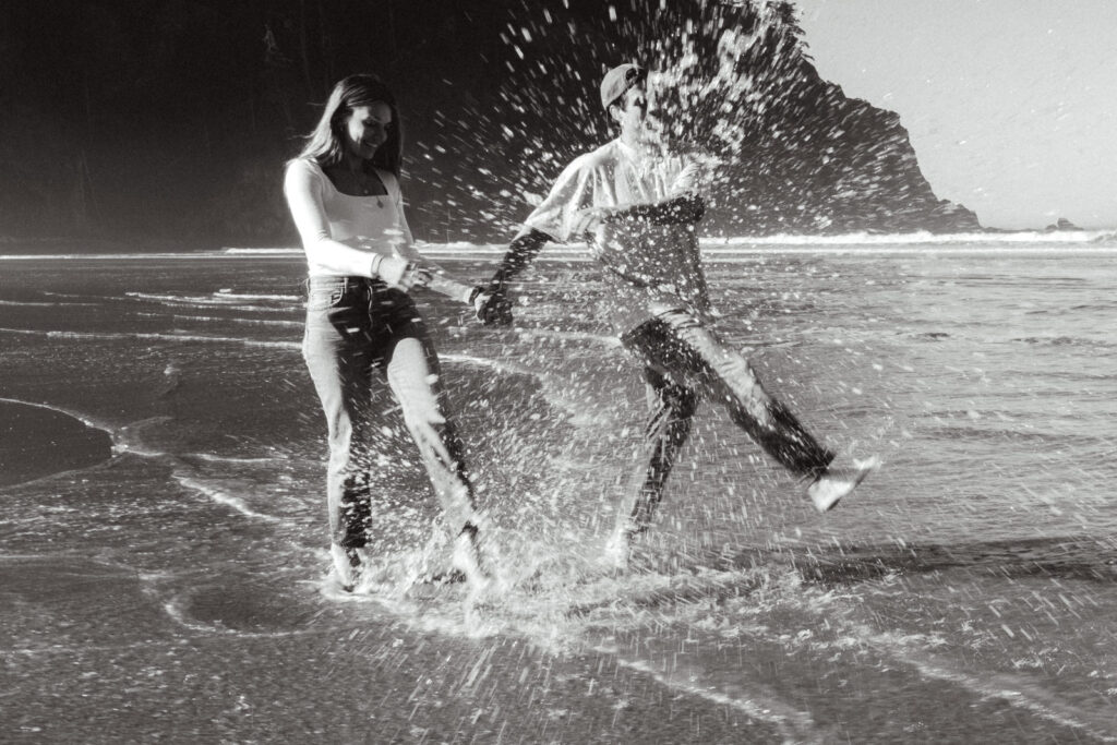during the morning of their coastal elopement, a bride and groom kick up ocean water with their feet 