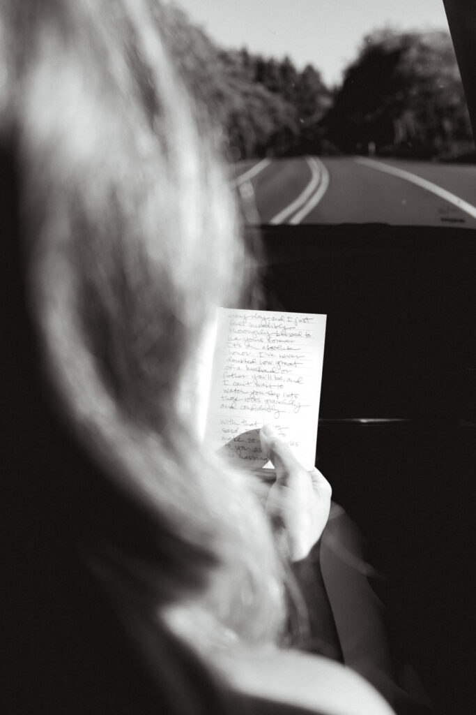A black and white image of a bride reading over her vows while driving to her coastal elopement.