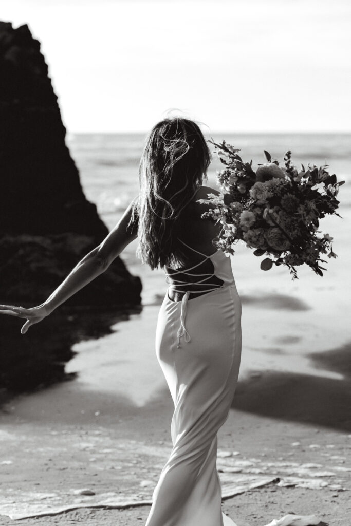 During her coastal elopement, a bride twirls with her bouquet. 