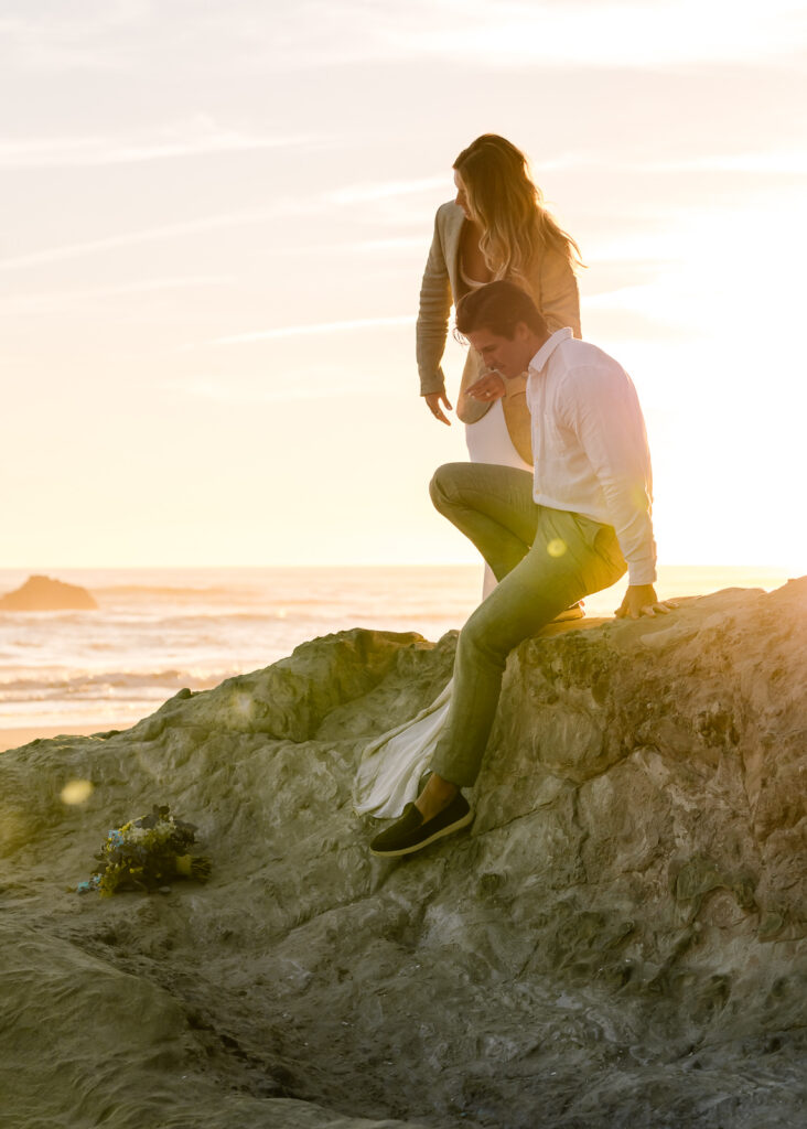 During their coastal elopement, a bride and groom explore a rocky beach during sunset. 