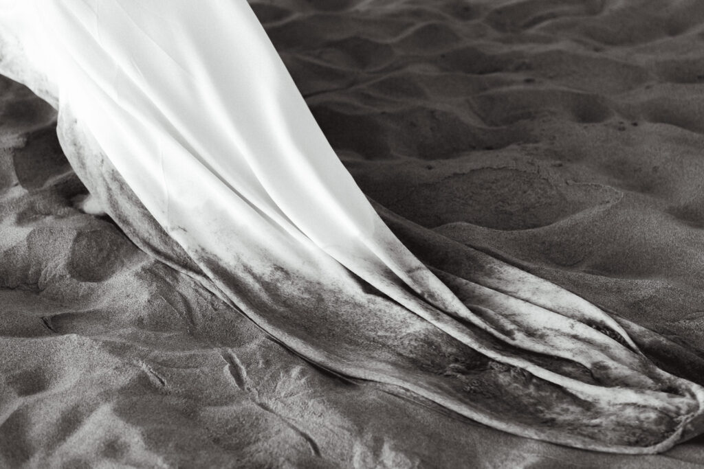 During her coastal elopement, the train of the brides dress moves through the sand