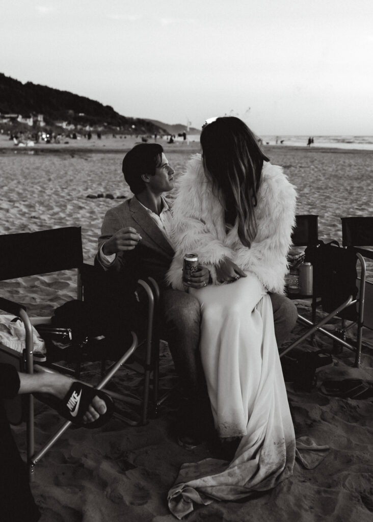 After their coastal elopement, a bride and groom share a chair at their bonfire beach reception.