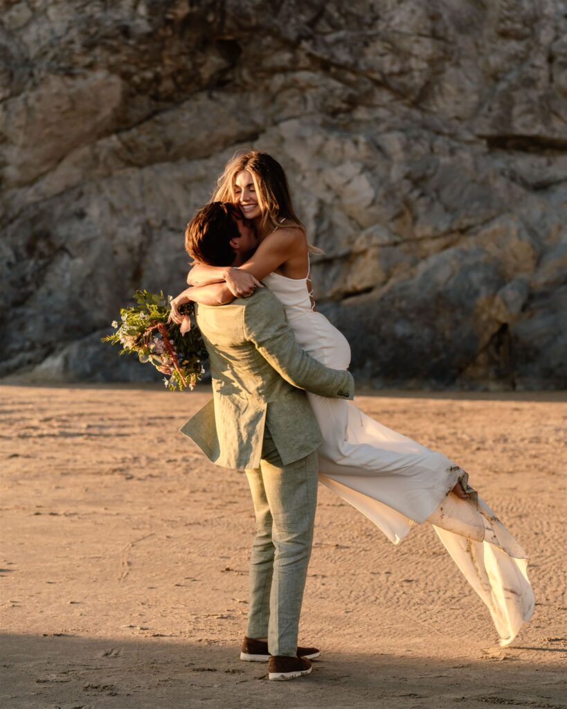 during their coastal elopement, a groom twirls his bride on the sunlit beach. 