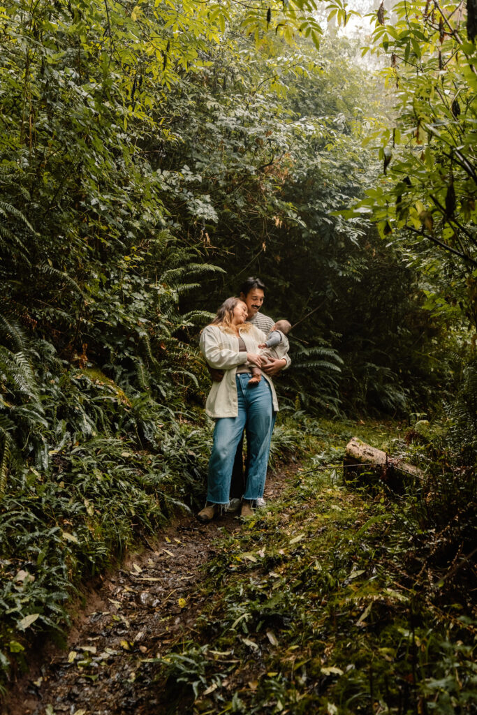 A family hikes and pauses together holding their baby as the lush greenery surrounds them