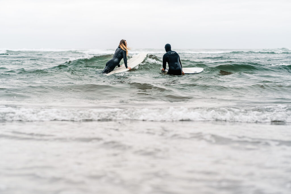 during their surfer wedding, a couple paddles out to catch a small wave on their boards. 