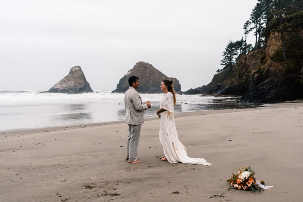 A bride and groom exchange vows on a moody beach during their surfer elopement. It is raining heavily, but they are thrilled. 