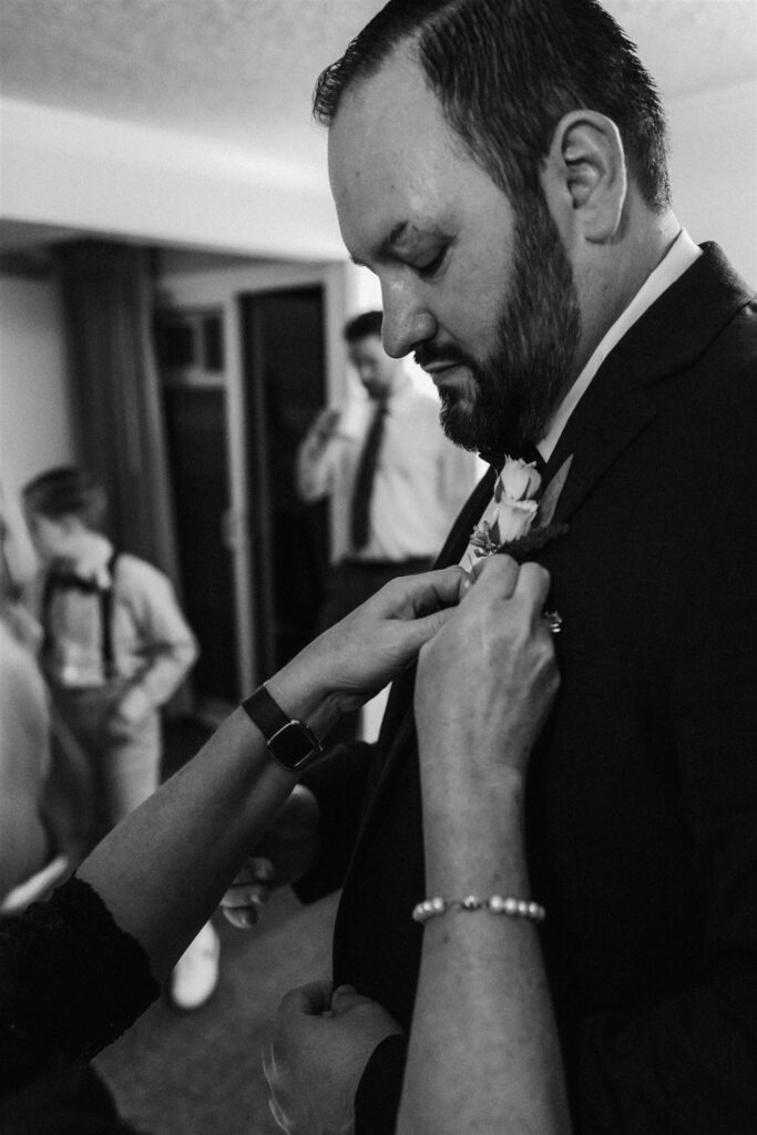 A mother fastens the boutonnière onto her sons suit jacket as he gets ready. 