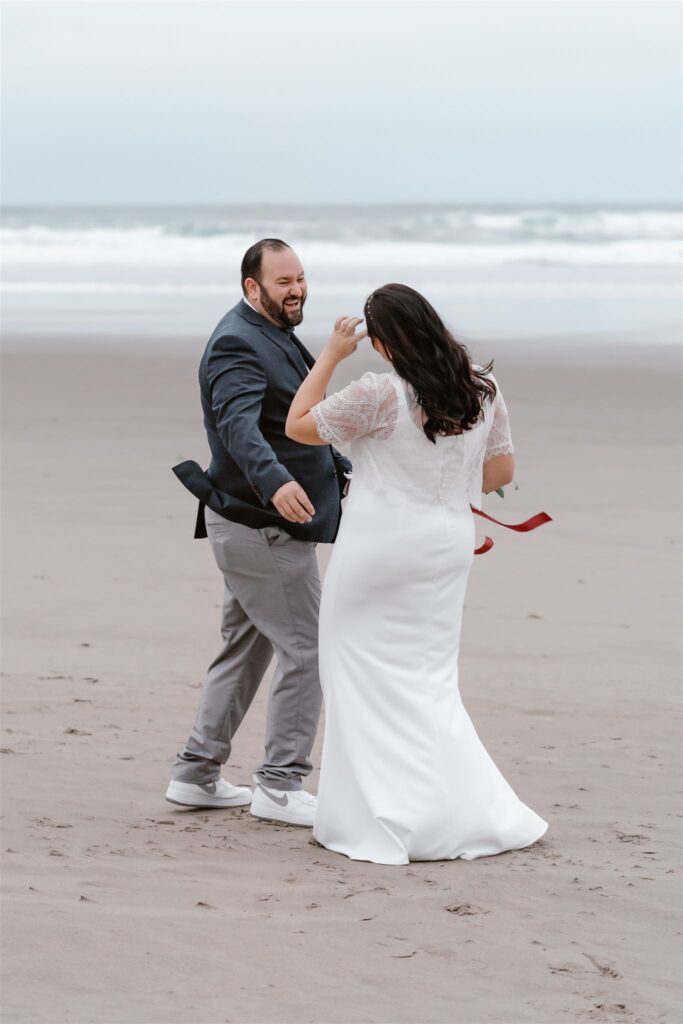 a groom smiles and laughs joyfully as he sees his bride in her dress for the first time during their Pacific coast wedding 