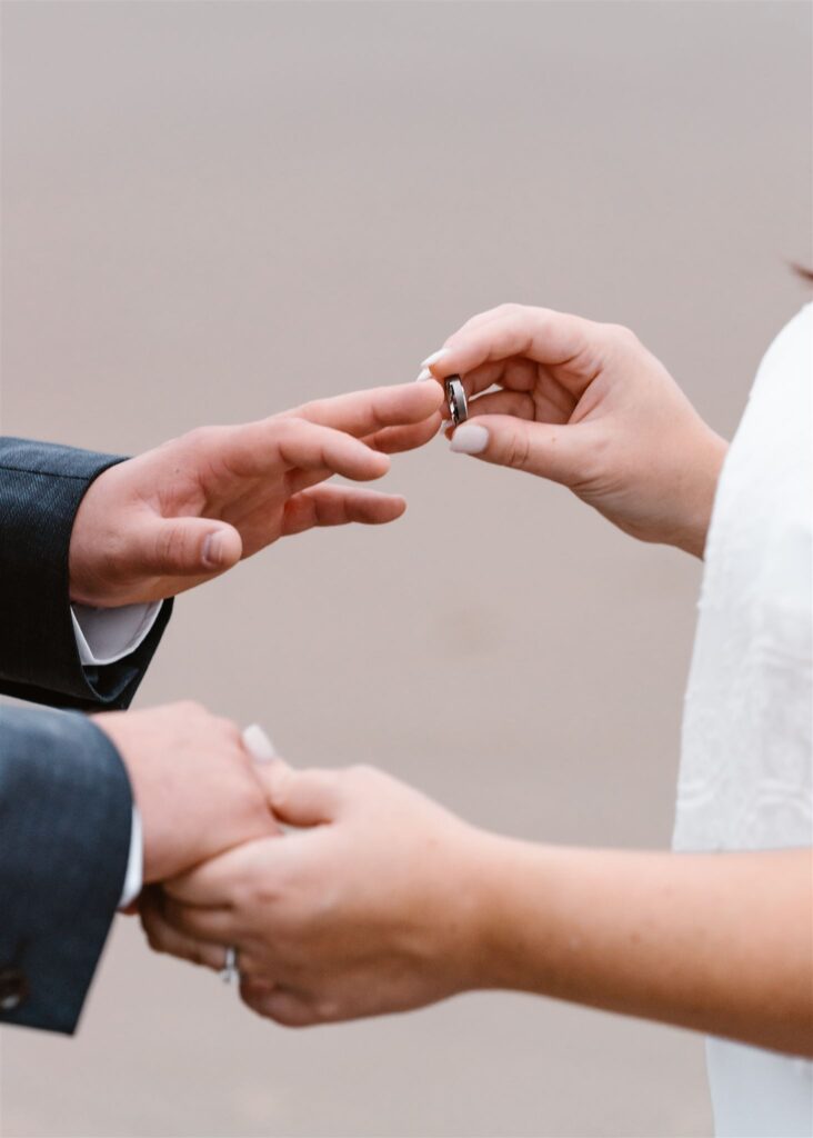 a close up shot of a bride placing the wedding band on her grooms finger 