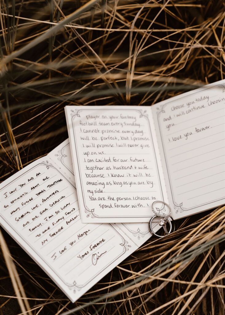 a detail shot of this couples vow books laying displayed in the sea grass. their wedding bands lay on top of them 