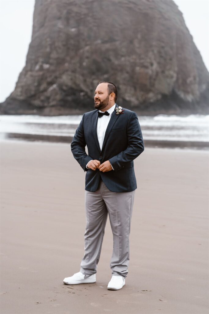 a groom fastens his suit jacket and smiles as he looks out during his pacific coast wedding