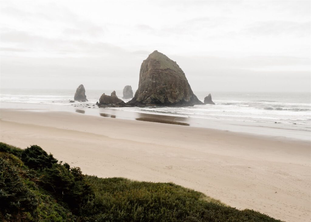 An empty beach with a large haystack rock.
