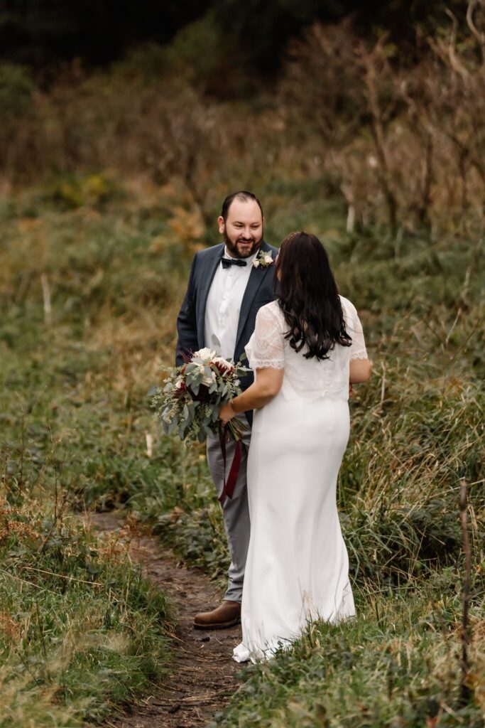 a groom smiles at his bride on a green trail as they explore during their pacific coast wedding