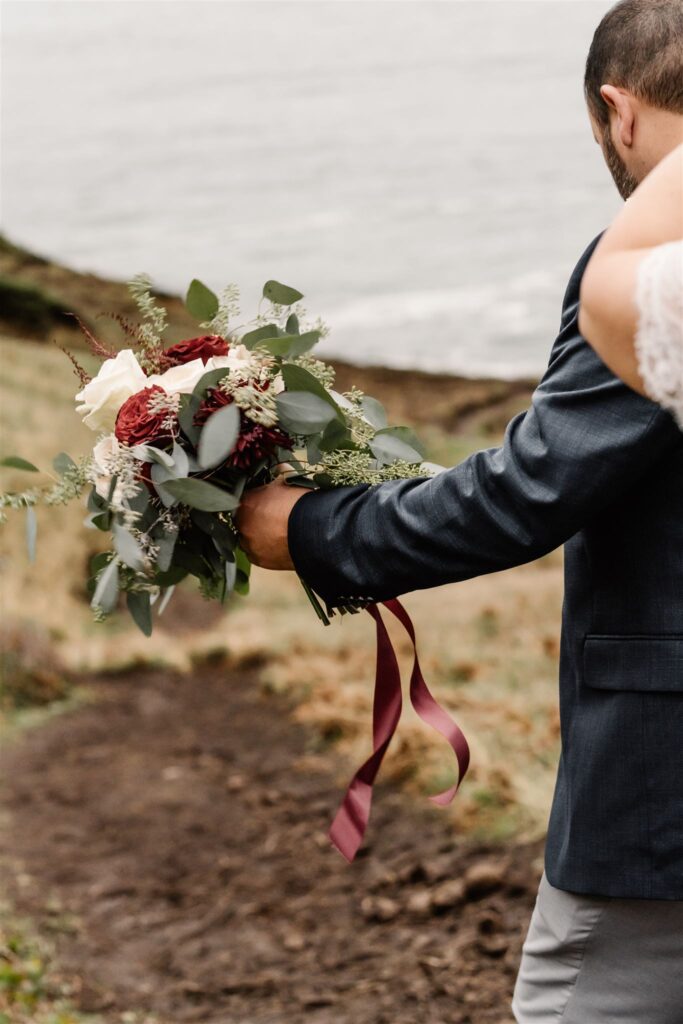 a close up shot of a bouquet being carried by the groom as he and his bride explore during their pacific coast wedding