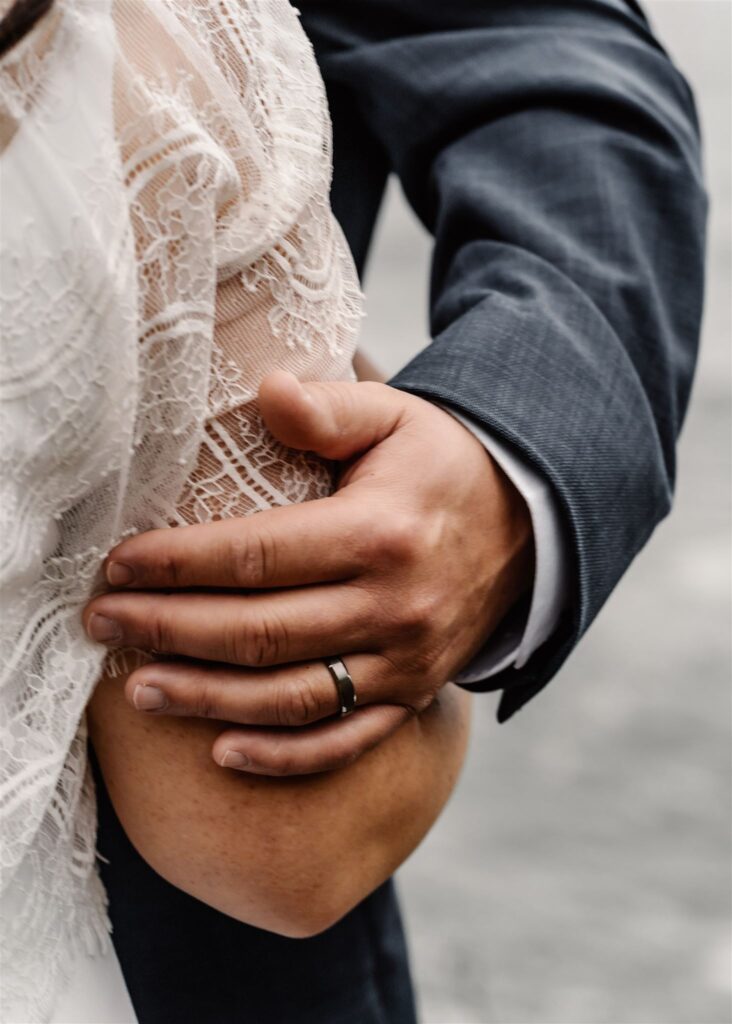 a close up shot of a groom lovingly holding his brides arm. they are embracing.