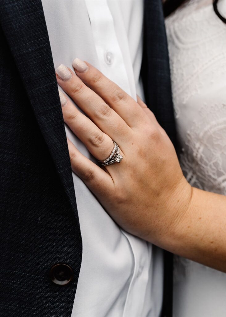 a close up shot of a brides ring on her hand. her hand rests on her grooms chest