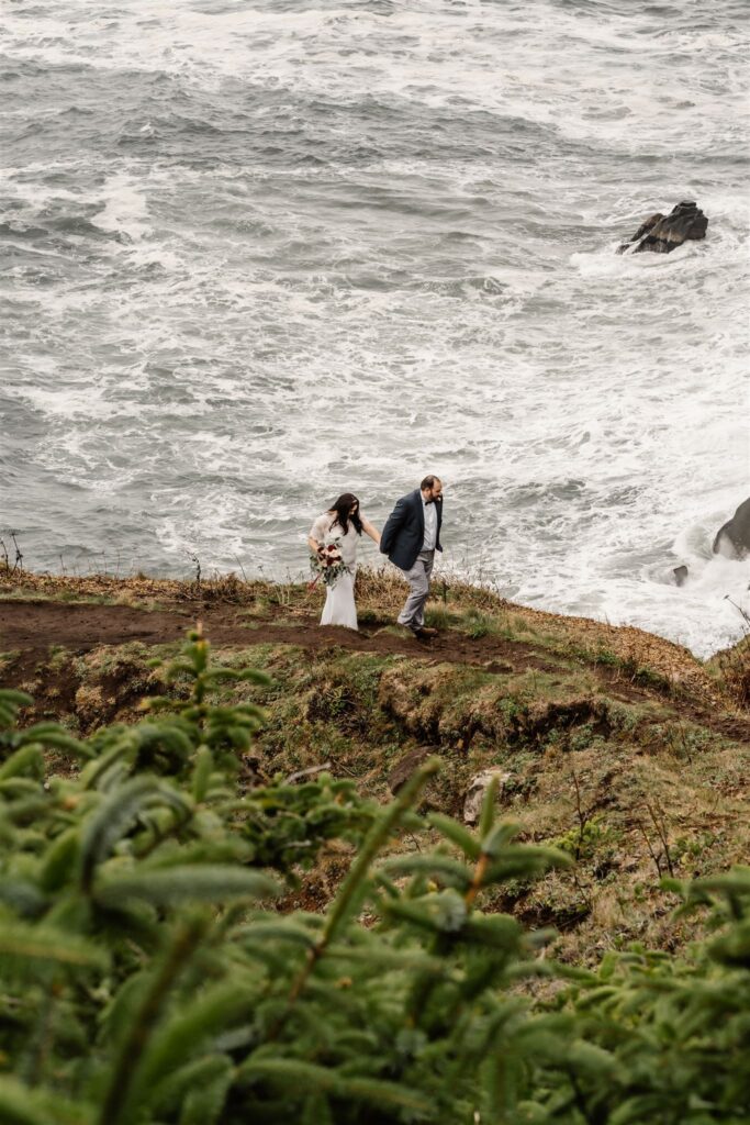 during their pacific coast wedding explores a coastal cliff looking over the ocean.