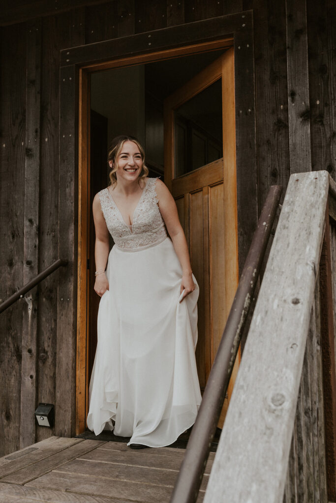 A giddy bride smiles with joy as she peeks out of the doorway to meet her groom for their first look before setting off for their forest wedding.