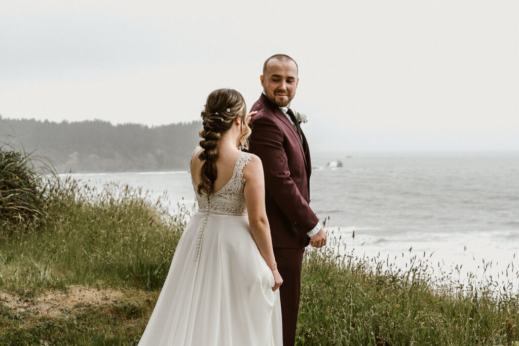 A bride turns her groom around. He smiles as he sees her 