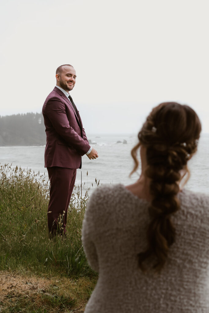 Shot over the shoulder of our bride, groom gives a cheeky smile to her as he tweaks his suit for their forest wedding.