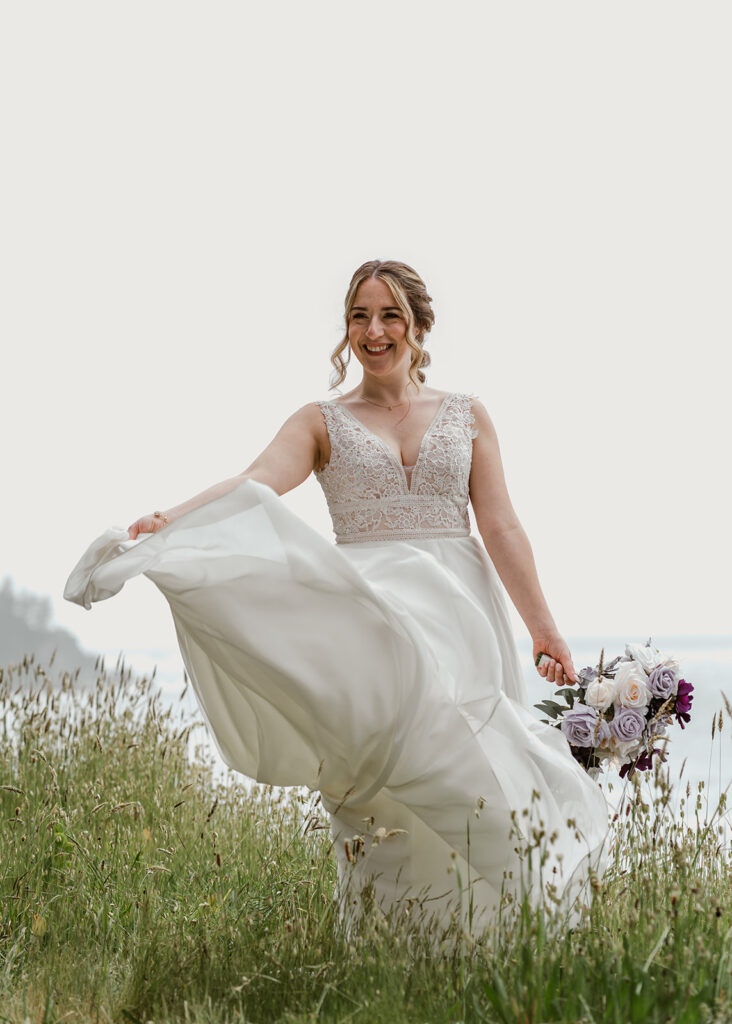 A bride twirls her dress among the tall grass, clutching her bouquet in her hand. She smiles wide at her groom as they prepare for their forest wedding