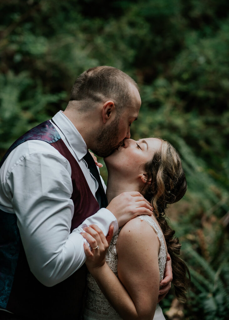 Under the soft light of the canopy, we see our bride and groom kiss passionately during their forest wedding 