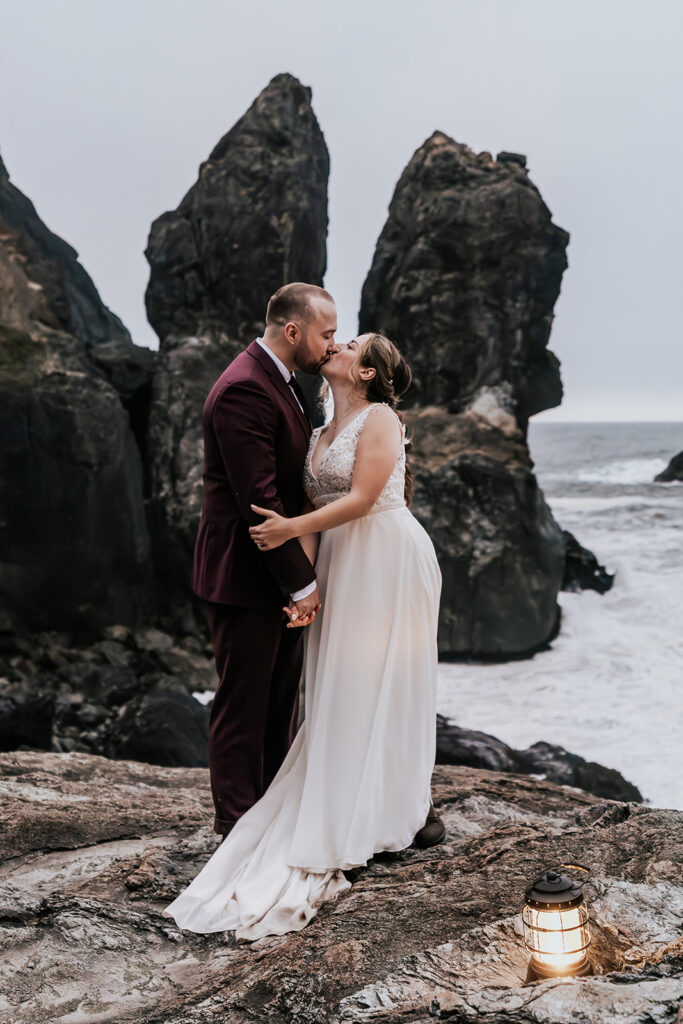 After their forest wedding, a bride and groom kiss in front of two huge vertical sea rocks