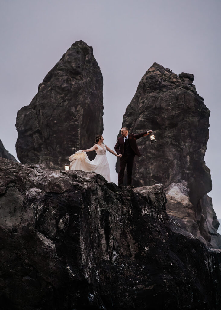 A bride and groom stand on massive sea rocks holding lanterns and dancing after their forest wedding