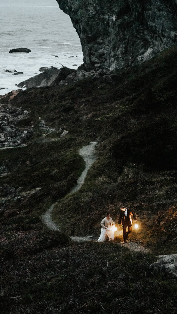 A groom leads his bride up a trail holding lanterns to give them light