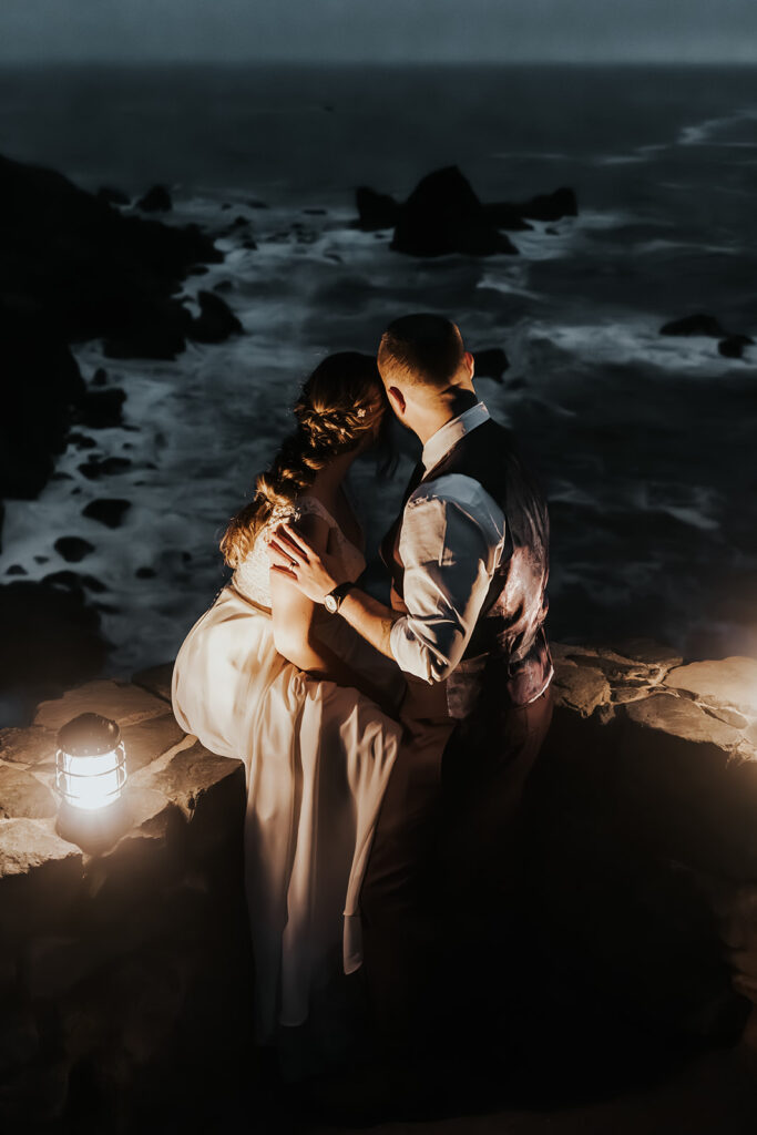 Gazing out at the sea, our bride and groom end their forest wedding by the light of just lanterns, embracing each other 