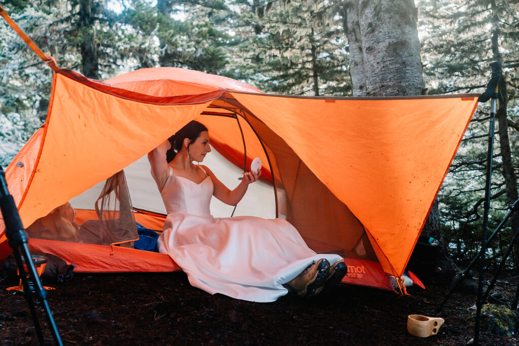 A bride, in her wedding dress, finishes getting ready for her backpacking wedding in a bright, orange tent 