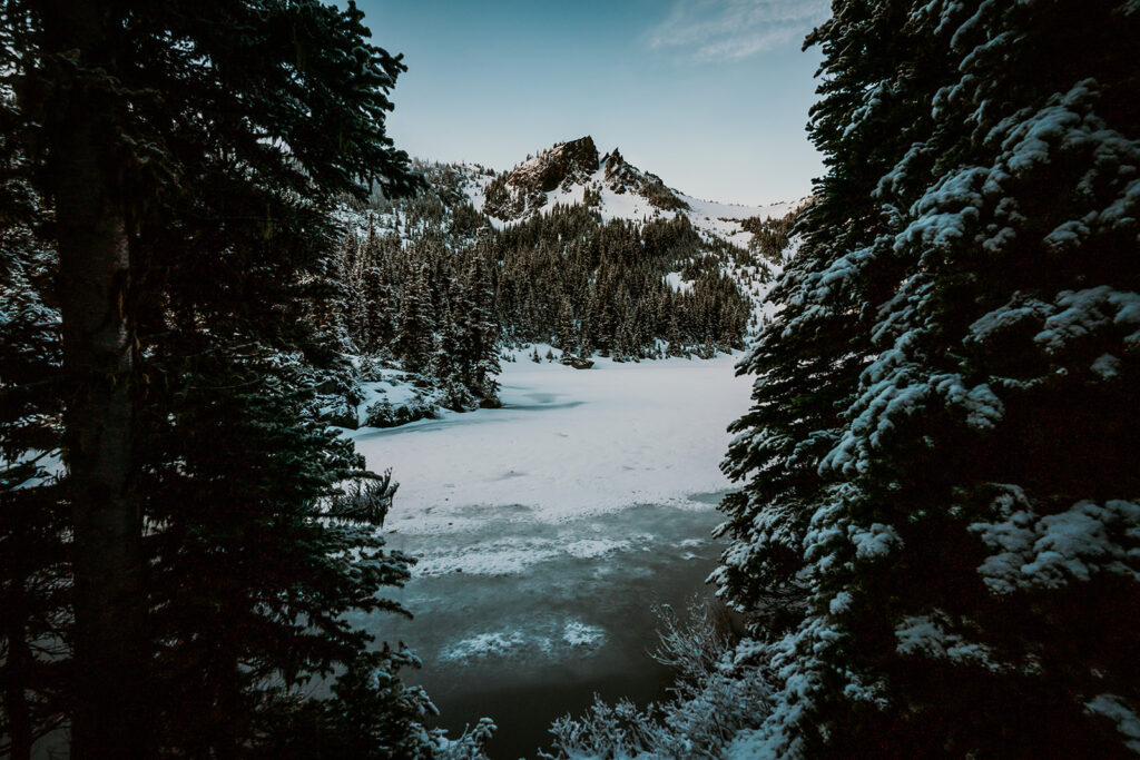 a landscape shot showing off the location for this backpacking wedding. An icy lake is surrounded by snowy mountains, pines, and blanketed in fresh snow