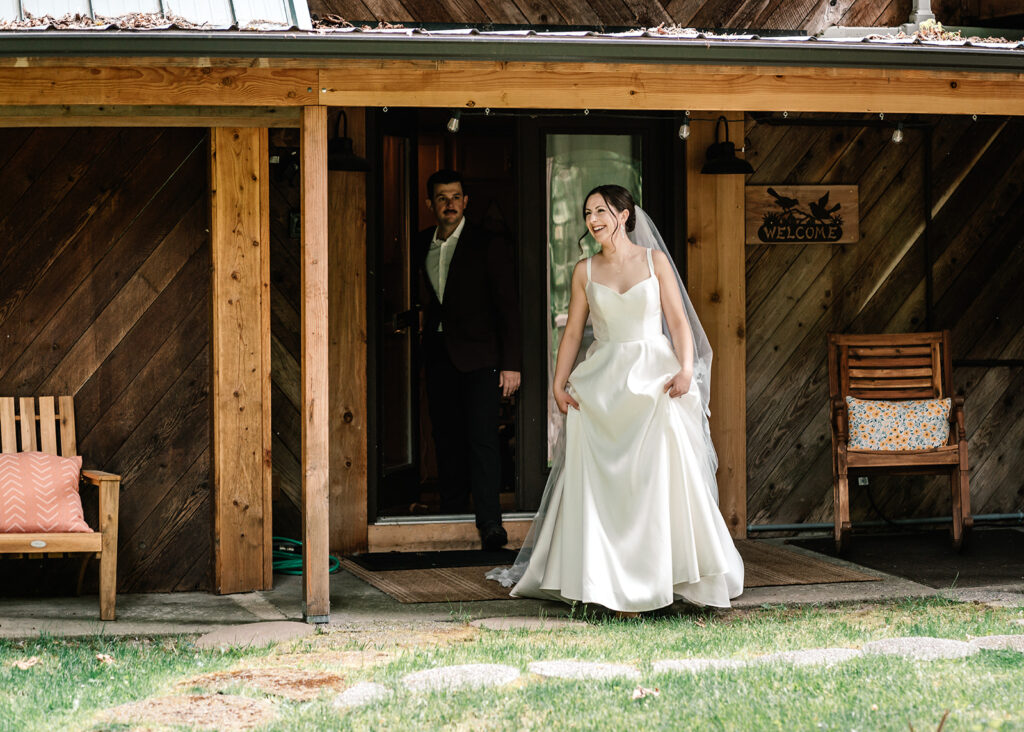 during their backpacking wedding, a couple walks outside their cabin in their wedding attire. They smile widely as they greet their guests for the first time