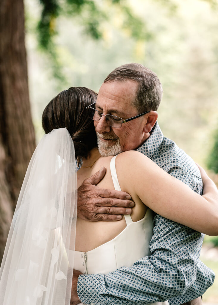 A bride embraces her father during her backpacking wedding.