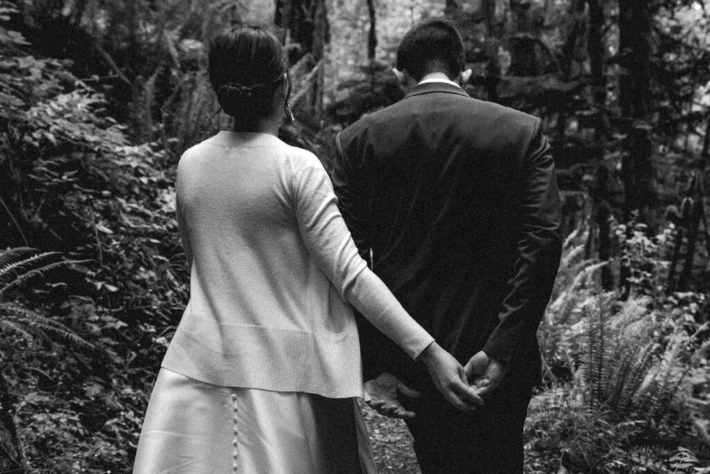 during their backpacking wedding, a bride and groom, in their wedding attire, walk with their hands intertwined behind them