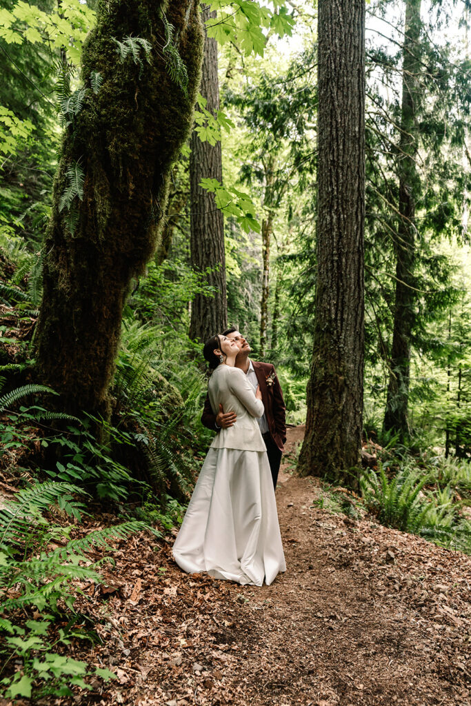 during their backpacking wedding, a bride and groom, in their wedding attire, stop a long the trail to admire the lush canopy 