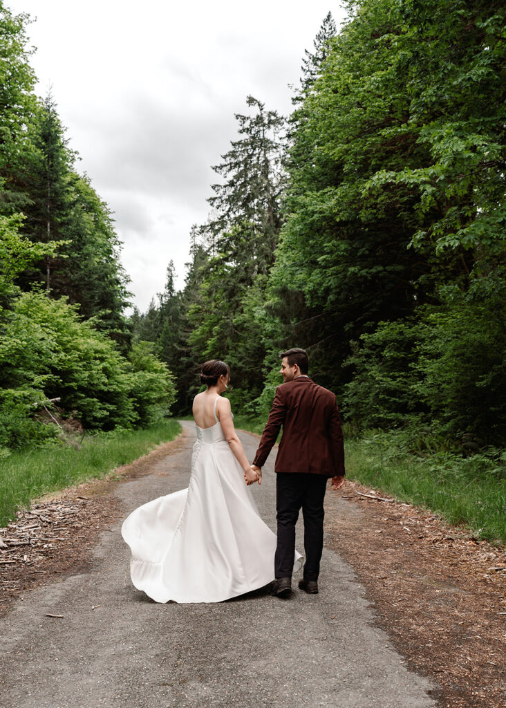 during their backpacking elopement, a bride and groom walk down an old, washed out road. They walk hand in hand as the brides dress billows behind her