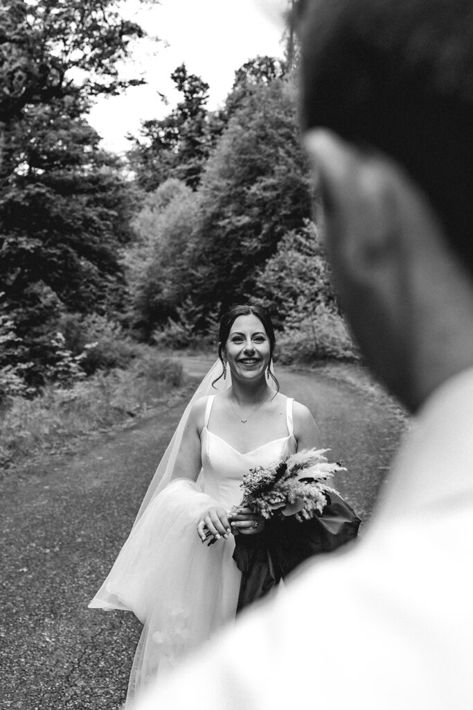 shot from over the grooms shoulder, we see his bride smiling widely at him during their backpacking wedding