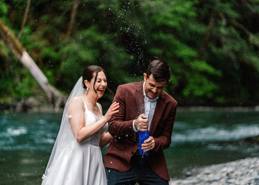 to celebrate their backpacking wedding, a bride and groom pop sparkling water on the rocky shore of the river