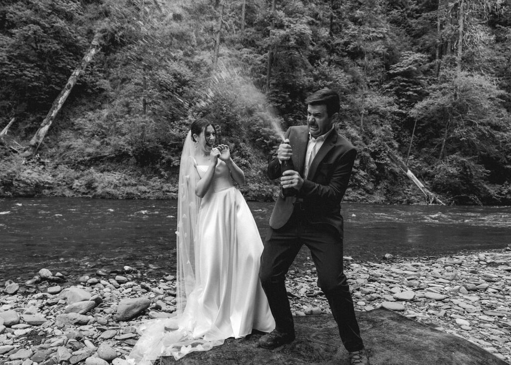 to celebrate their backpacking wedding, a bride and groom pop sparkling water on the rocky shore of the river