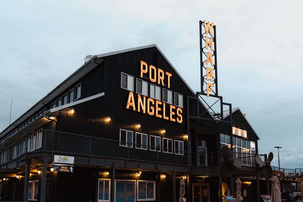 a landscape image of the large building on the wharf. bright letters read "Port Angeles Wharf" 