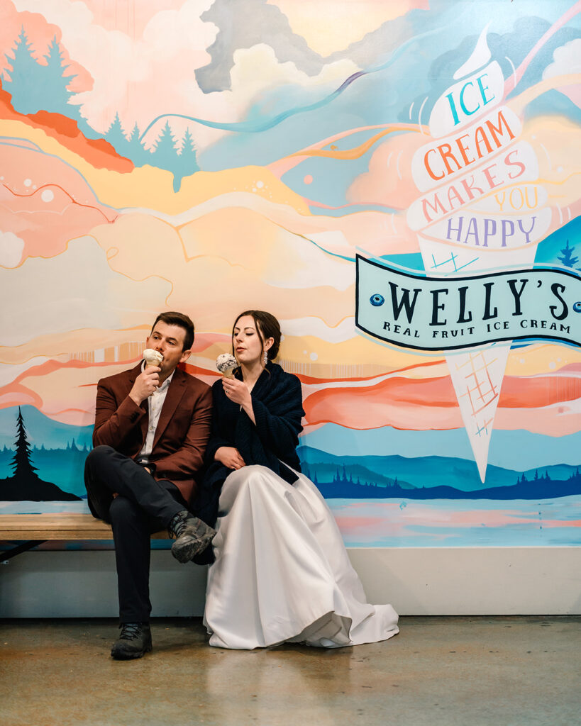 a bride and groom sit in front of a wall painted with bright colors. an ice bream cone is painted and reads "ice cream makes you happy" as a way to end their backpacking wedding 