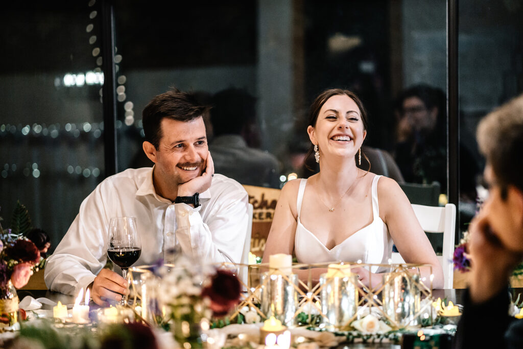 a bride and groom smile as they chat with their guests at dinner as they celebrate their backpacking wedding 