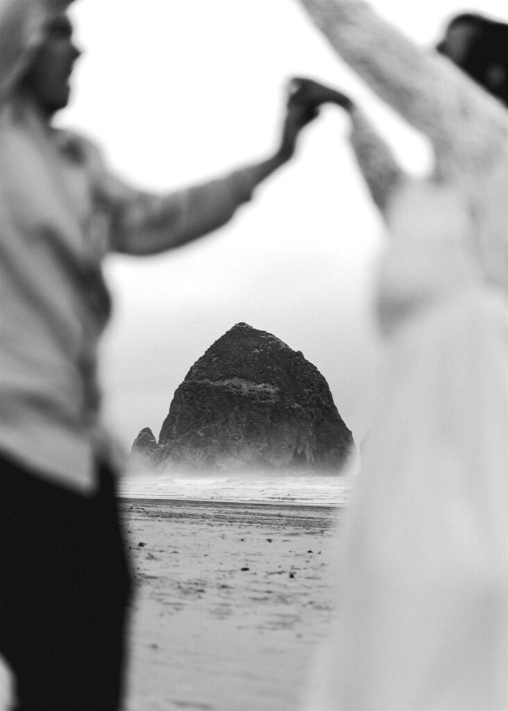 a shot of haystack rock framed by a bride and groom dancing after their elopement ceremony