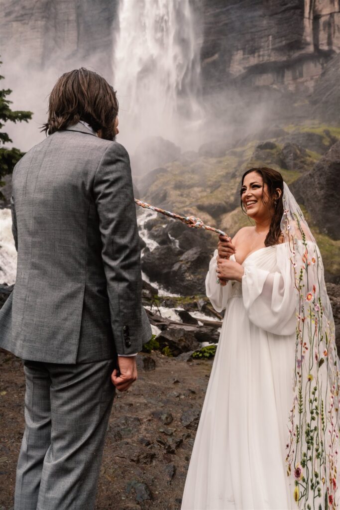 s bride smiles wide as she and her groom tighten the knot from their hand fasting elopement ceremony