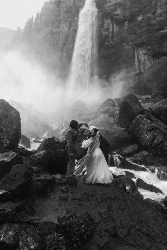 a black and white image of a bride and groom dancing under a waterfall. he spins her as they share their first dance after their elopement ceremony 