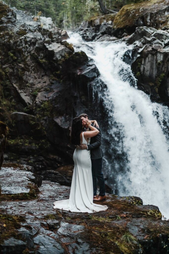 a bride and groom kiss in front of a gushing waterfall at the end of their elopement ceremony