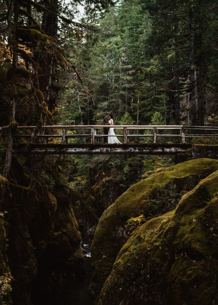 a bride and groom embrace on a wooden bridge surrounded by rocky boulders during their elopement ceremony 