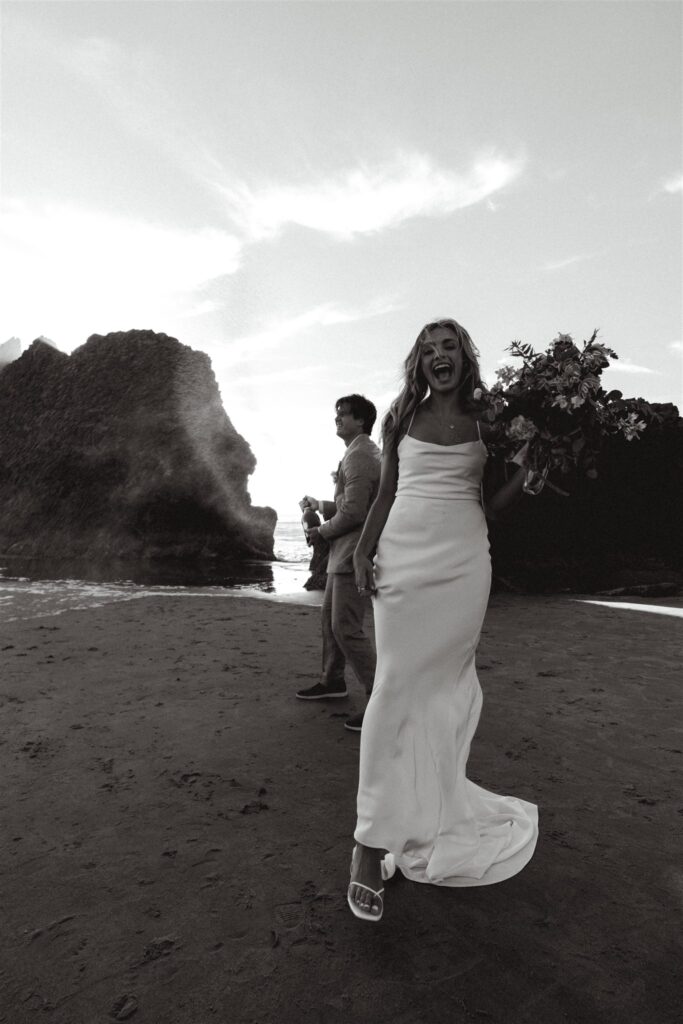 a black and white image of a bride smiling and cheering as her groom pops champagne behind her to celebrate their elopement ceremony