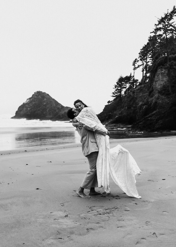 a groom picks up his bride and spins her around after their elopement ceremony on a moody, rocky beach 